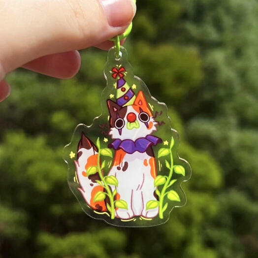 Image shows a hand holding a calico cat dressed as a clown keychain